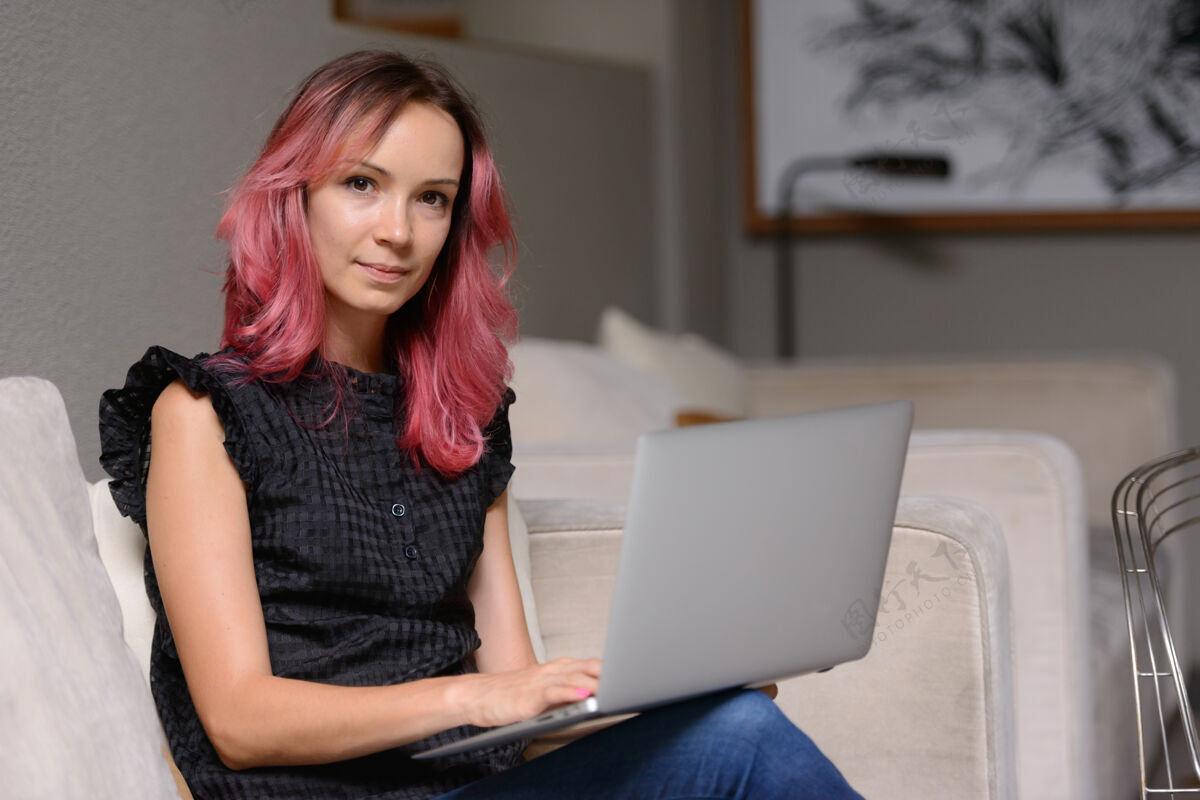 沙发美丽的商人肖像与粉红色的头发使用笔记本电脑在客厅从家办公的概念起居休闲室内