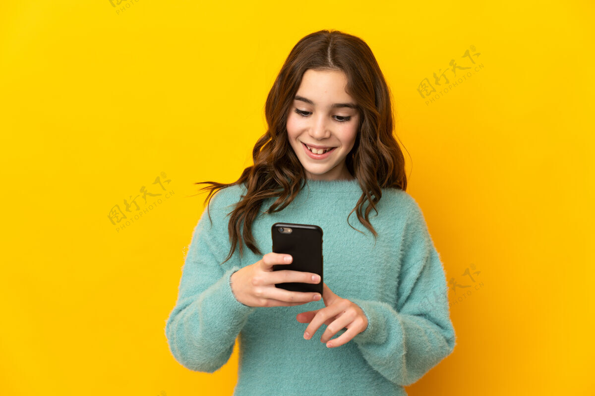童年被隔离在黄色背景下的白人小女孩用手机发送信息或电子邮件说话女性孩子
