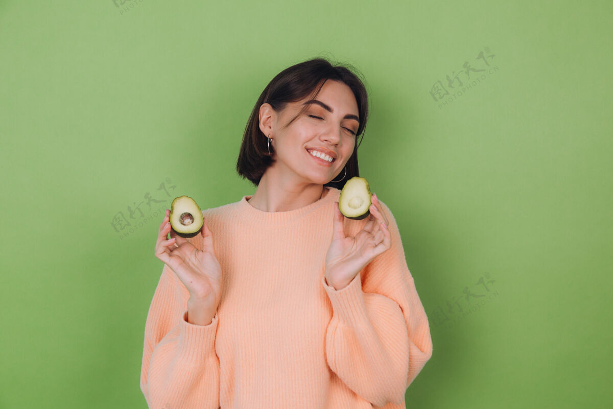 卡路里年轻女子穿着休闲桃毛衣隔离在绿橄榄墙上捧着鳄梨 健康护肤理念 复制空间蔬菜女人微笑
