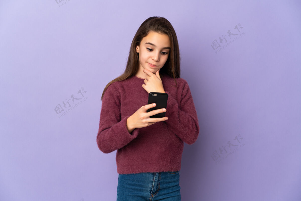 女孩小女孩孤零零地站在紫色的墙上思考着 发着信息手机小手势