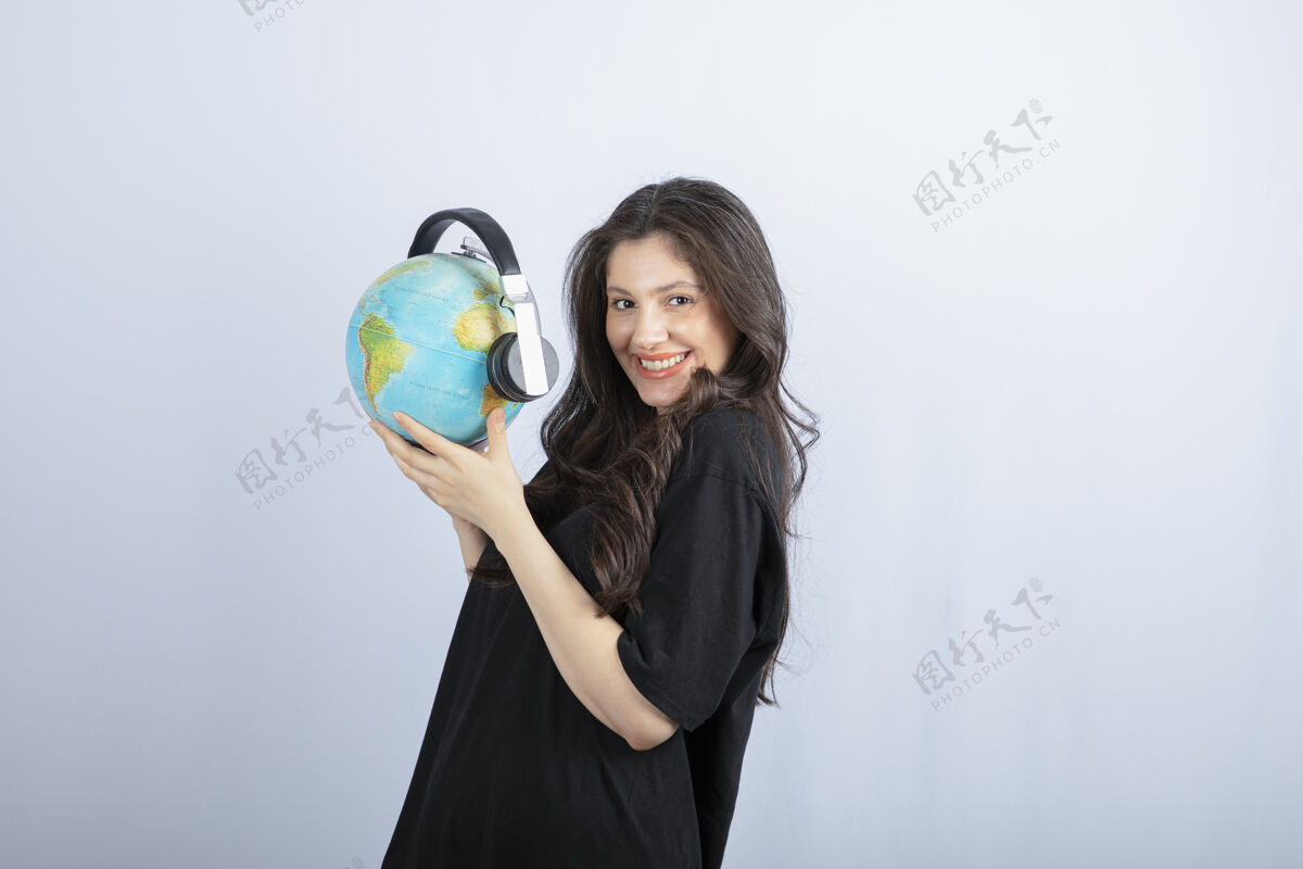 只有一个女性面带微笑的年轻女子戴着耳机站着拿着地球仪女人休闲女性