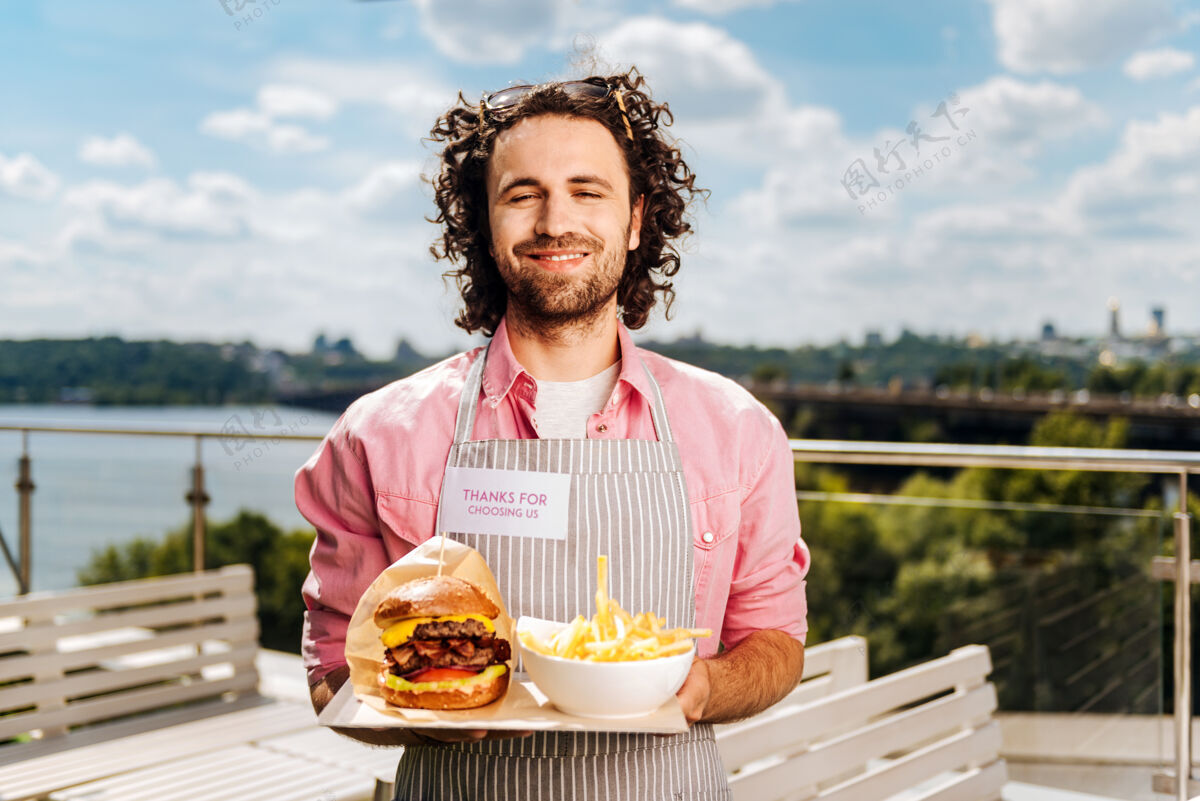 卡路里快餐有经验的卷发英俊的快餐工人为他的客户带来汉堡和薯条帅气河流汉堡