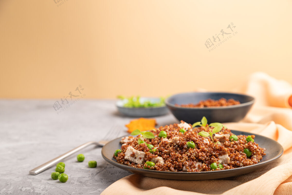 肉类奎奴亚藜麦片粥 绿色豌豆和鸡肉放在灰色混凝土表面和橙色织物上的陶瓷板上盘子谷物草药