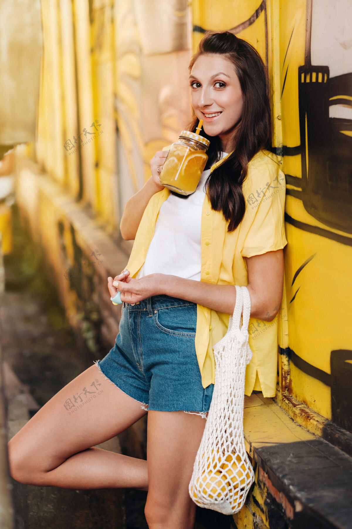 柠檬一个穿着黄色衬衫 短裤和黑色鞋子 网着柠檬和柠檬汁的女孩走在城市街道上一个手里拿着鸡尾酒的女人街头咖啡馆柠檬汁咖啡馆