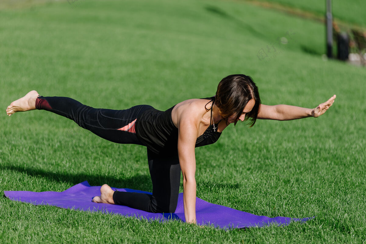 瑜伽女孩在公园的草地上练瑜伽夏天一个女人在公园里做体式早上运动瑜伽