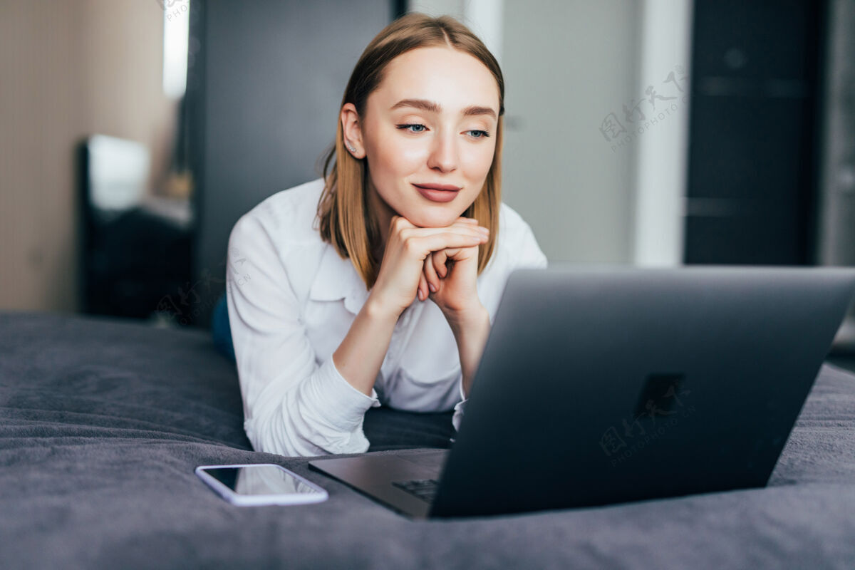 被子懒洋洋地躺在床上用笔记本电脑休息时 一个微笑着的女人在社交媒体上忙得不可开交枕头漂亮女性