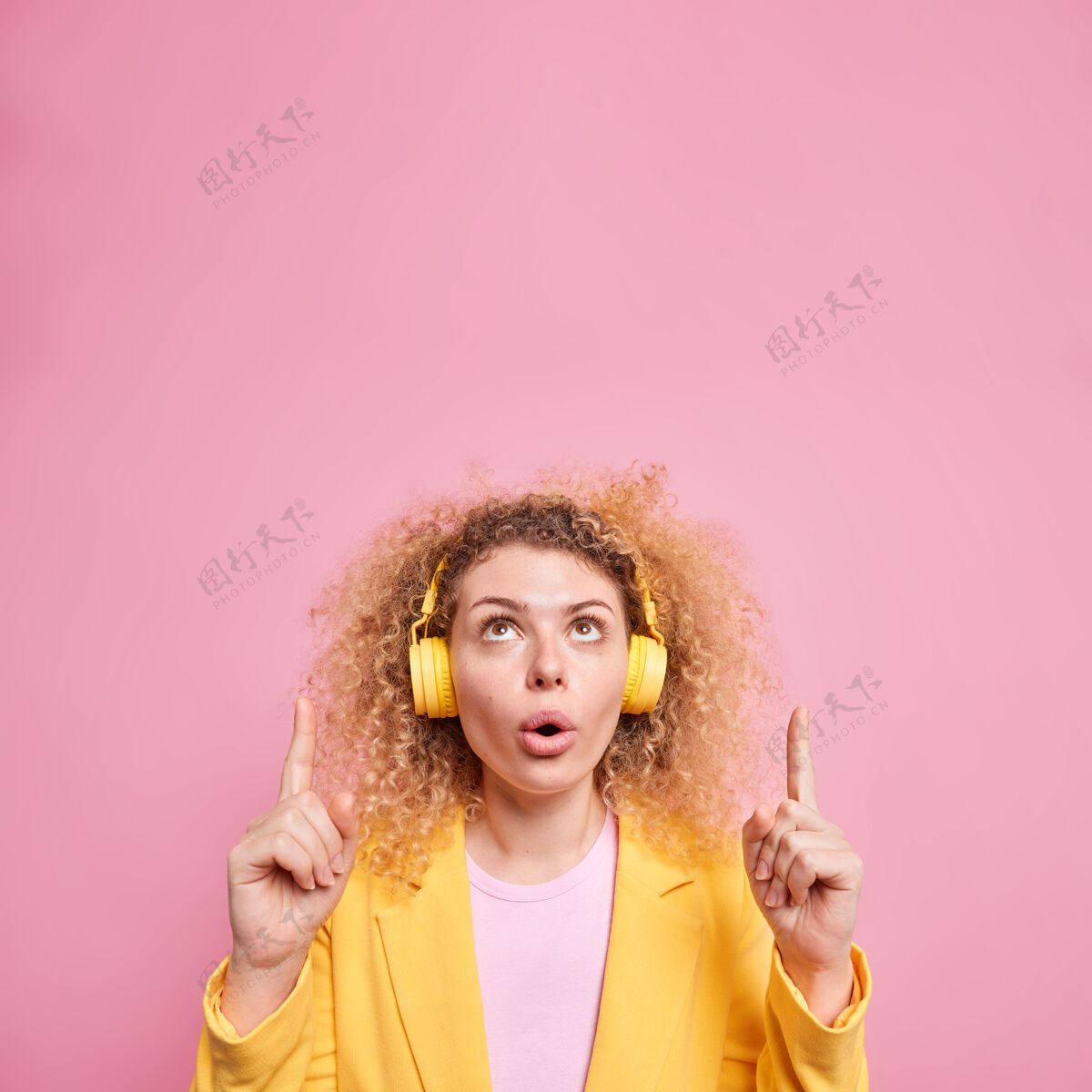 女性无言卷发女子的垂直镜头 表情惊异 向上展示了意想不到的报价 头顶戴着无线耳机 耳朵上放着最喜欢的播放列表头顶正式惊呆