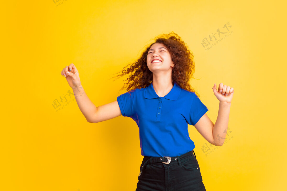 手与飞舞的头发跳舞黄色工作室背景上的白人少女肖像美丽的女性卷发模型人类情感的概念 面部表情 销售 广告 教育复制空间卷发人女孩