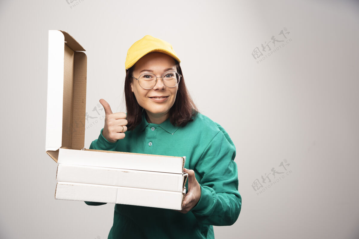 人女送货员竖起大拇指 拿着一张白色的高质量照片上的比萨饼卡片美味芳香帽子