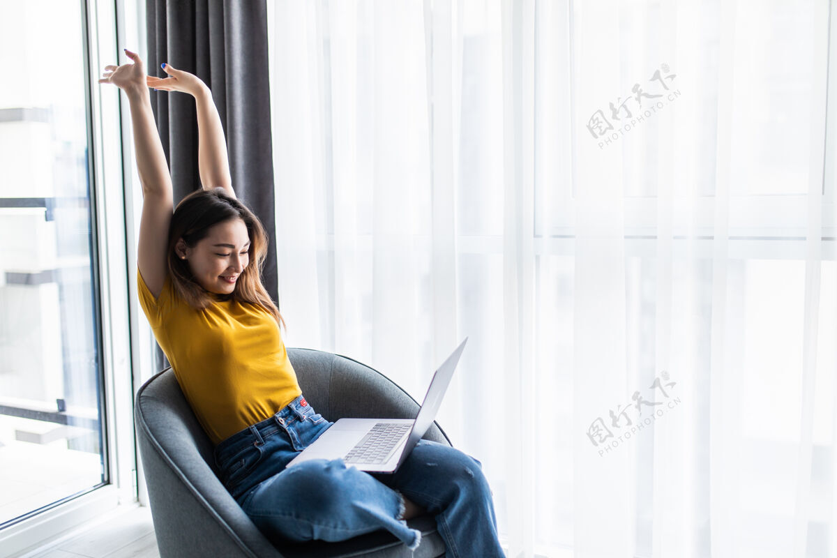 电脑快乐轻松的休闲女人坐在椅子上 面前放着一台笔记本电脑 双臂伸过头顶压力笔记本椅子