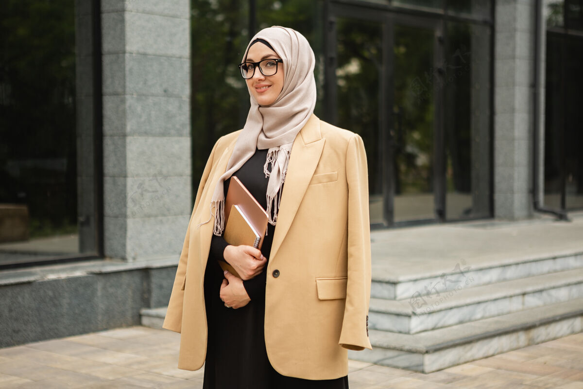 女性现代时尚的穆斯林妇女戴着头巾 穿着商务风格的夹克和黑色的长袍 带着笔记本电脑走在城市街道上自信头巾伊斯兰
