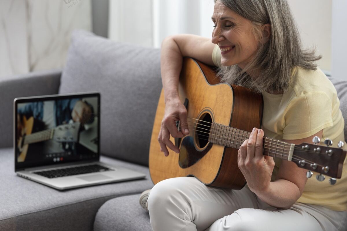 成人资深女士在家沙发上用笔记本电脑上吉他课老年人女性老年人