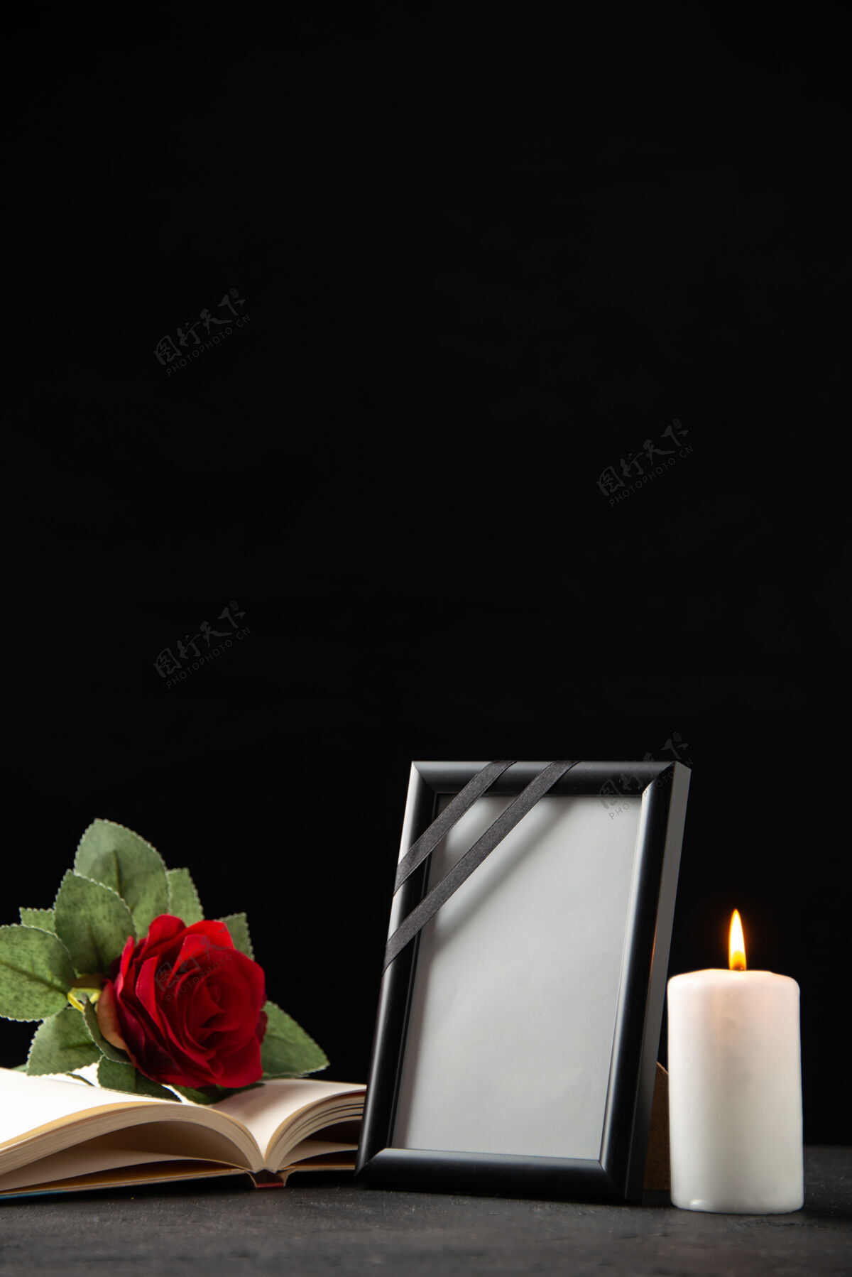 葬礼红玫瑰的正面图 黑色的书和画框叶子打蜡蜡烛