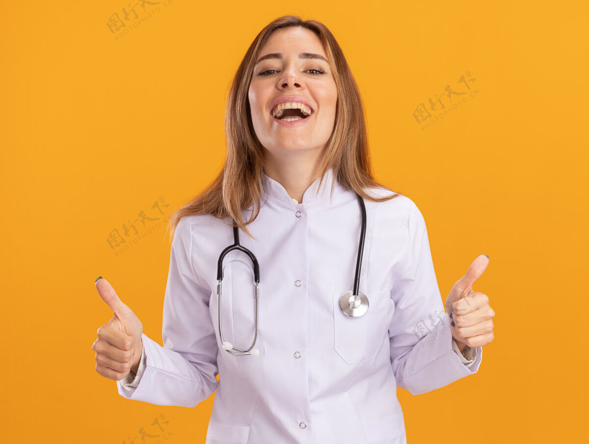 人笑着的年轻女医生穿着医用长袍 听诊器在黄色的墙上竖起大拇指女性人感觉