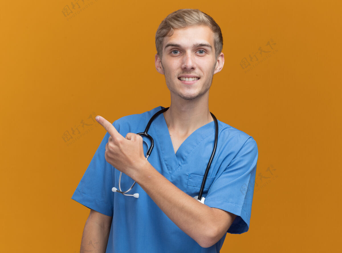 站微笑的年轻男医生穿着医生制服 听诊器指向隔离在橙色墙壁上的一侧 留有复印空间感觉壁板衣服