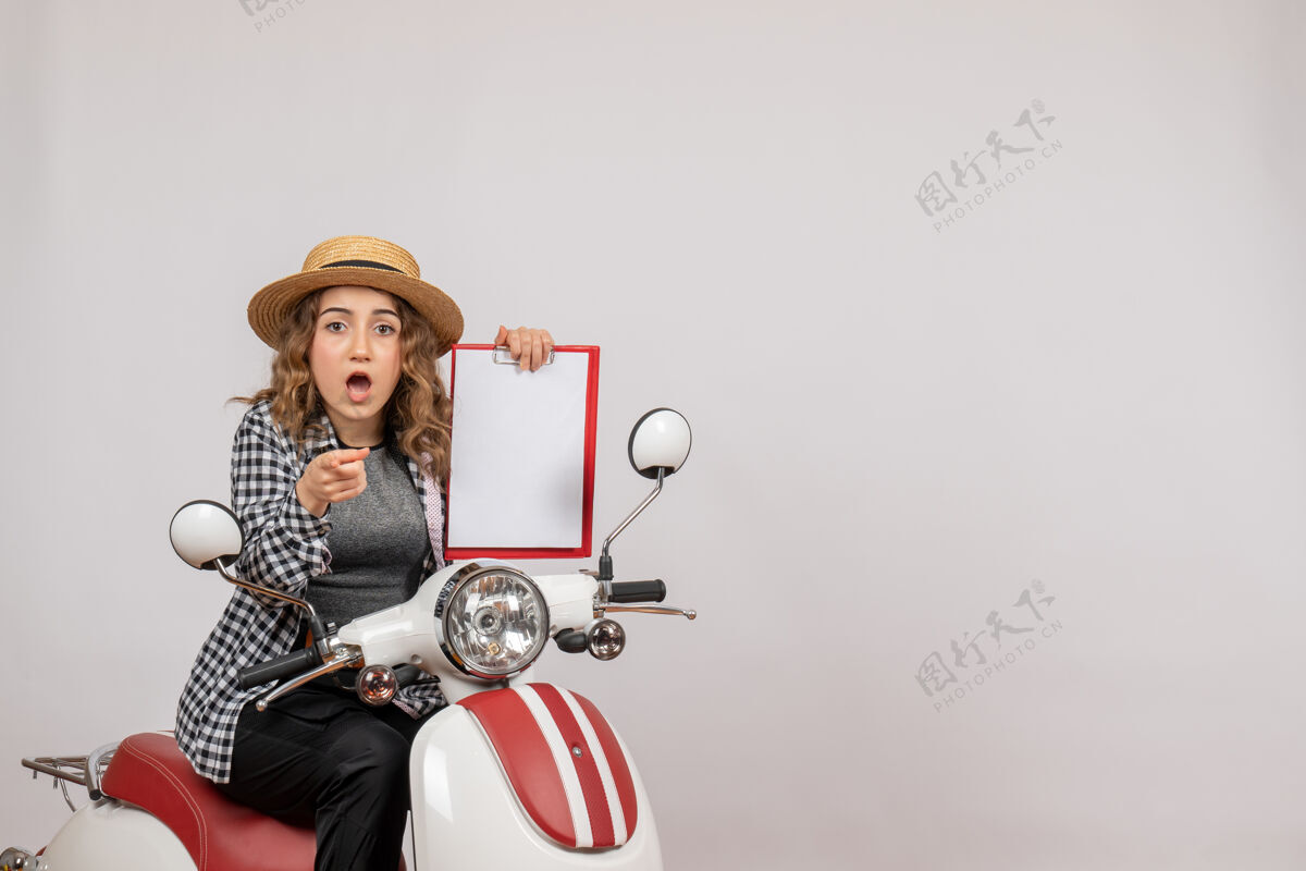 车辆前视图骑着轻便摩托车的年轻女孩举着剪贴板指着前面剪贴板人举行