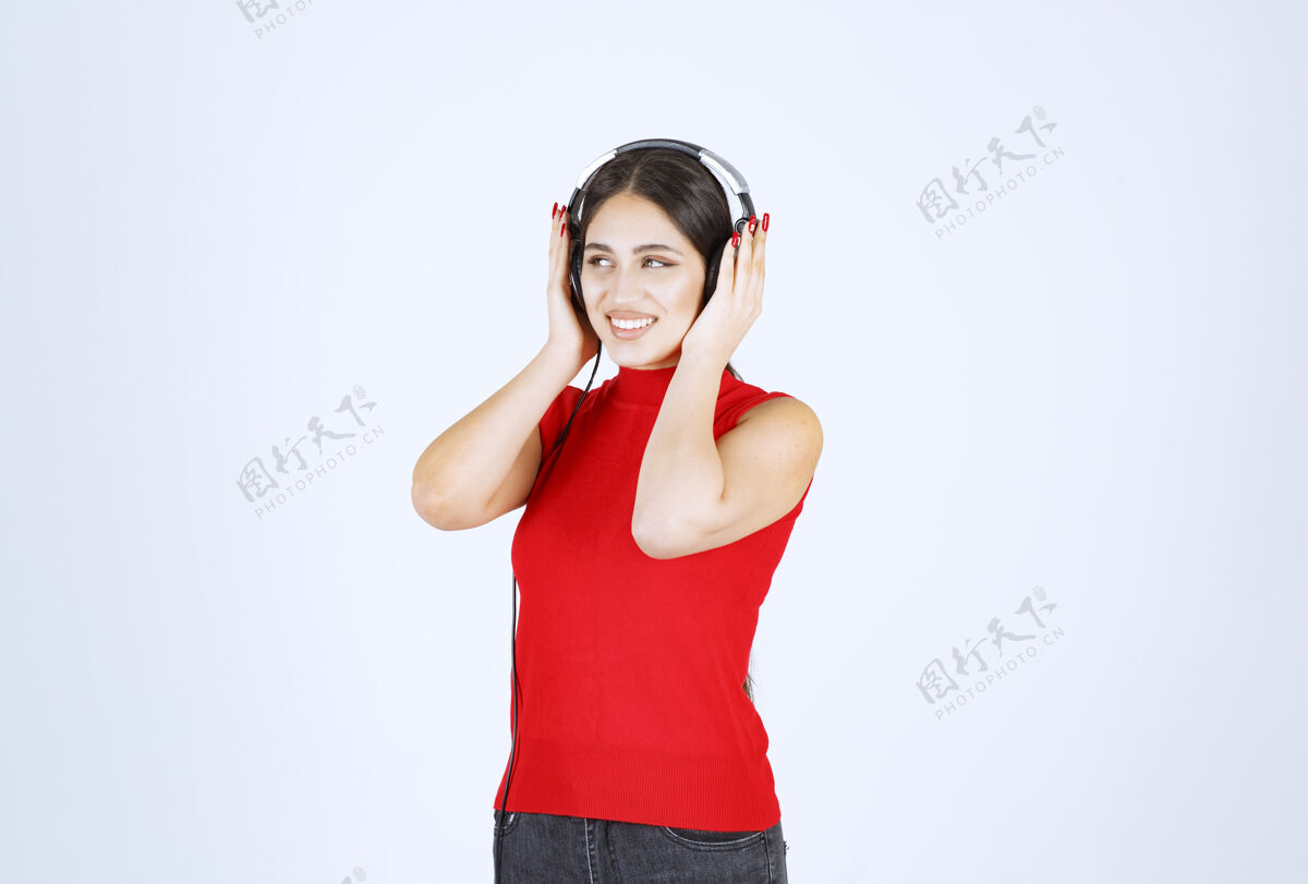 享受穿着红衬衫的Dj女孩戴着耳机 听着好听的音乐成人女人场景