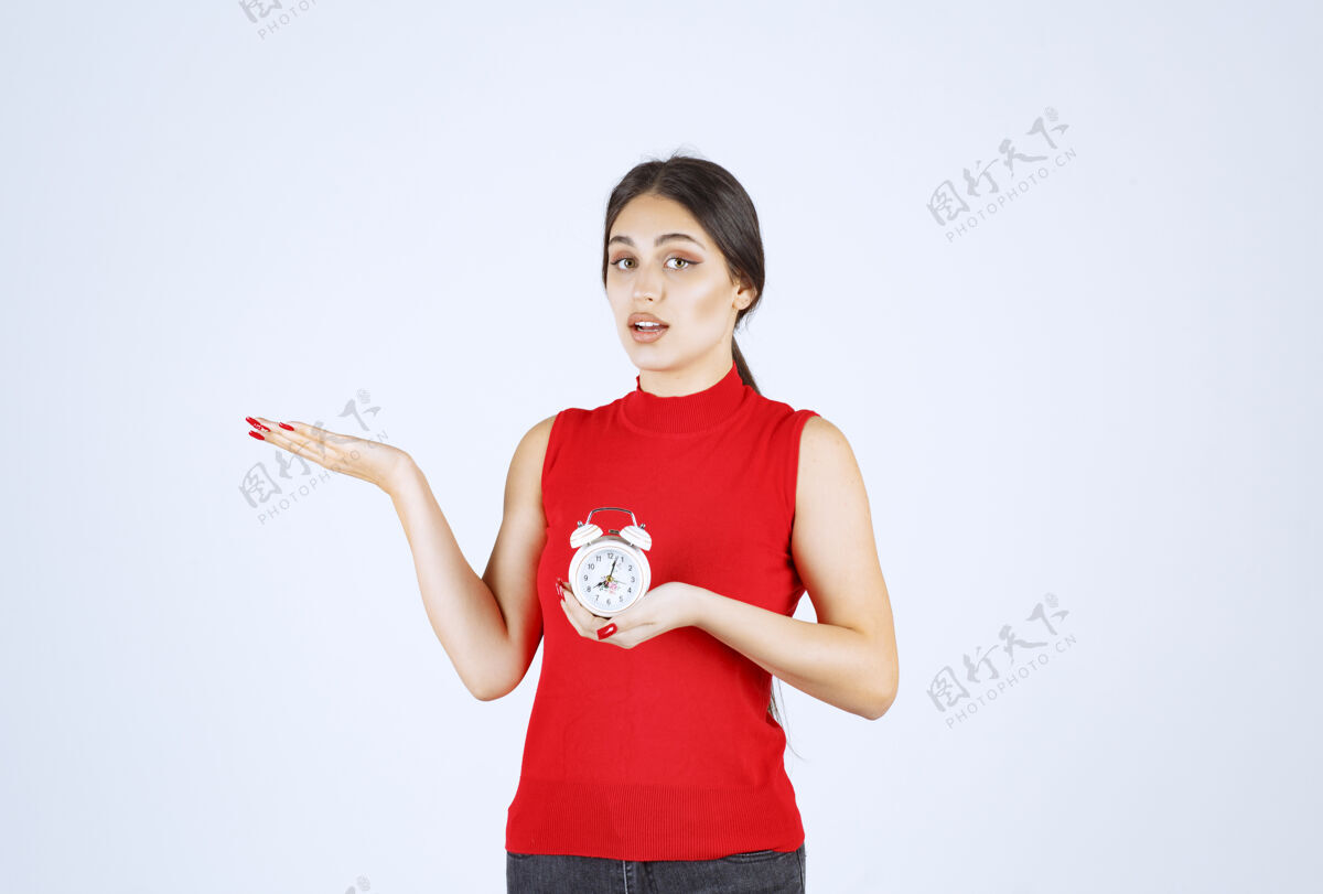 女性穿红衬衫的女孩拿着闹钟 推销着闹钟人成人姿势