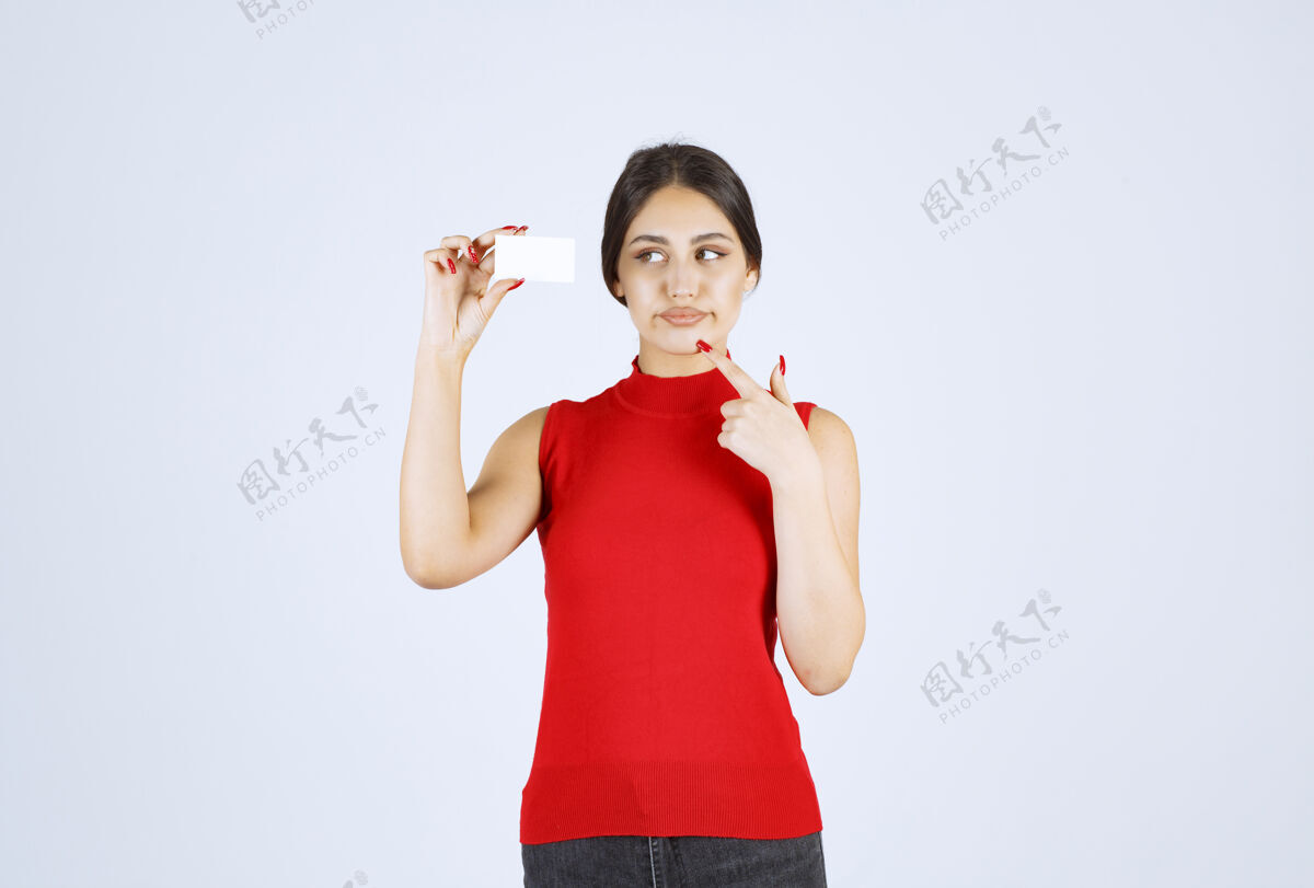 模特一个穿着红衫的女孩拿着一张名片 看上去很困惑 很不满意年轻人压力姿势