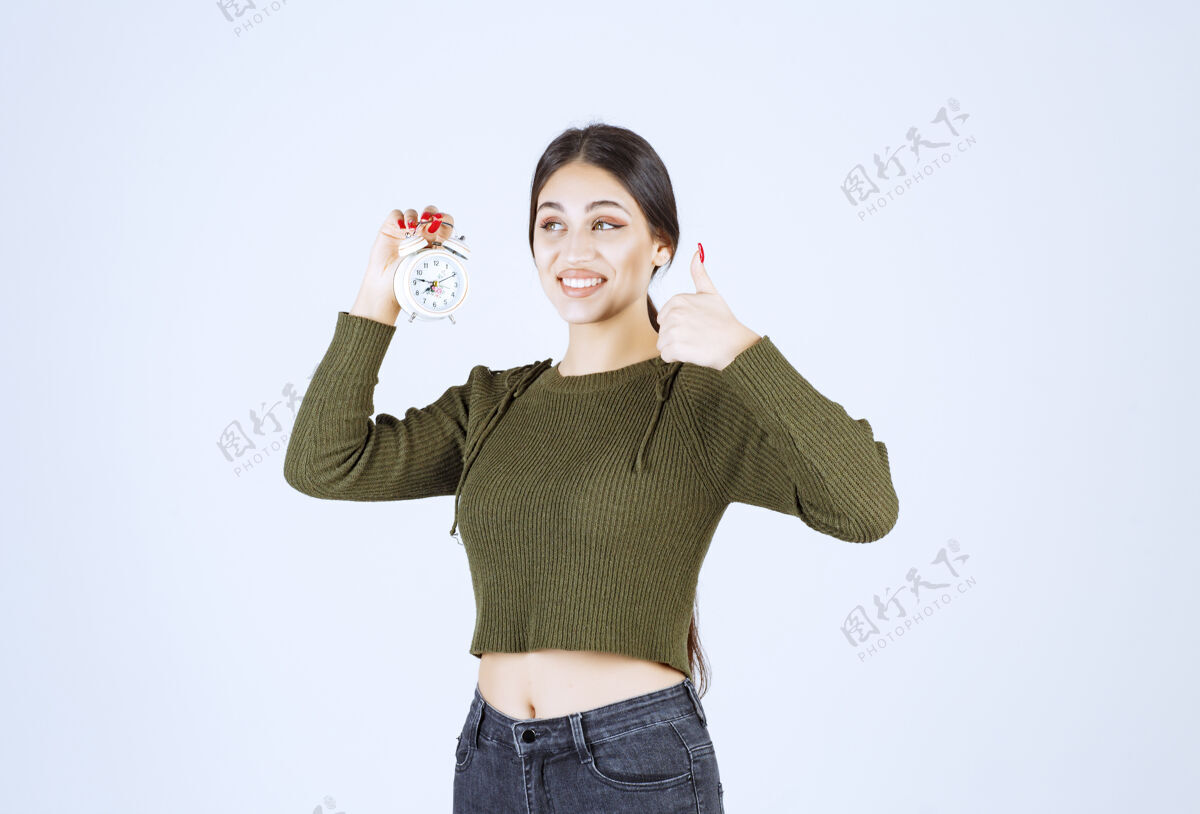 闹钟年轻漂亮的女人拿着闹钟竖起大拇指秀手势肖像