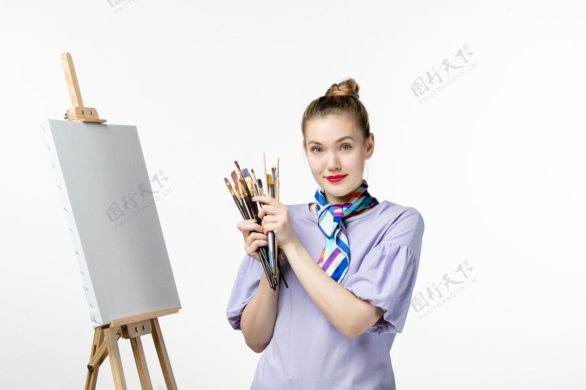 前面正面图女画家拿着流苏在白墙上画架上画画女人画艺术照片画铅笔女人视图绘画