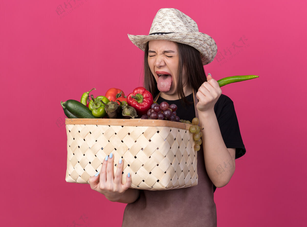 卡住漂亮的白人女园丁戴着园艺帽 伸着舌头 手里拿着菜篮子和辣椒花园粉红胡椒