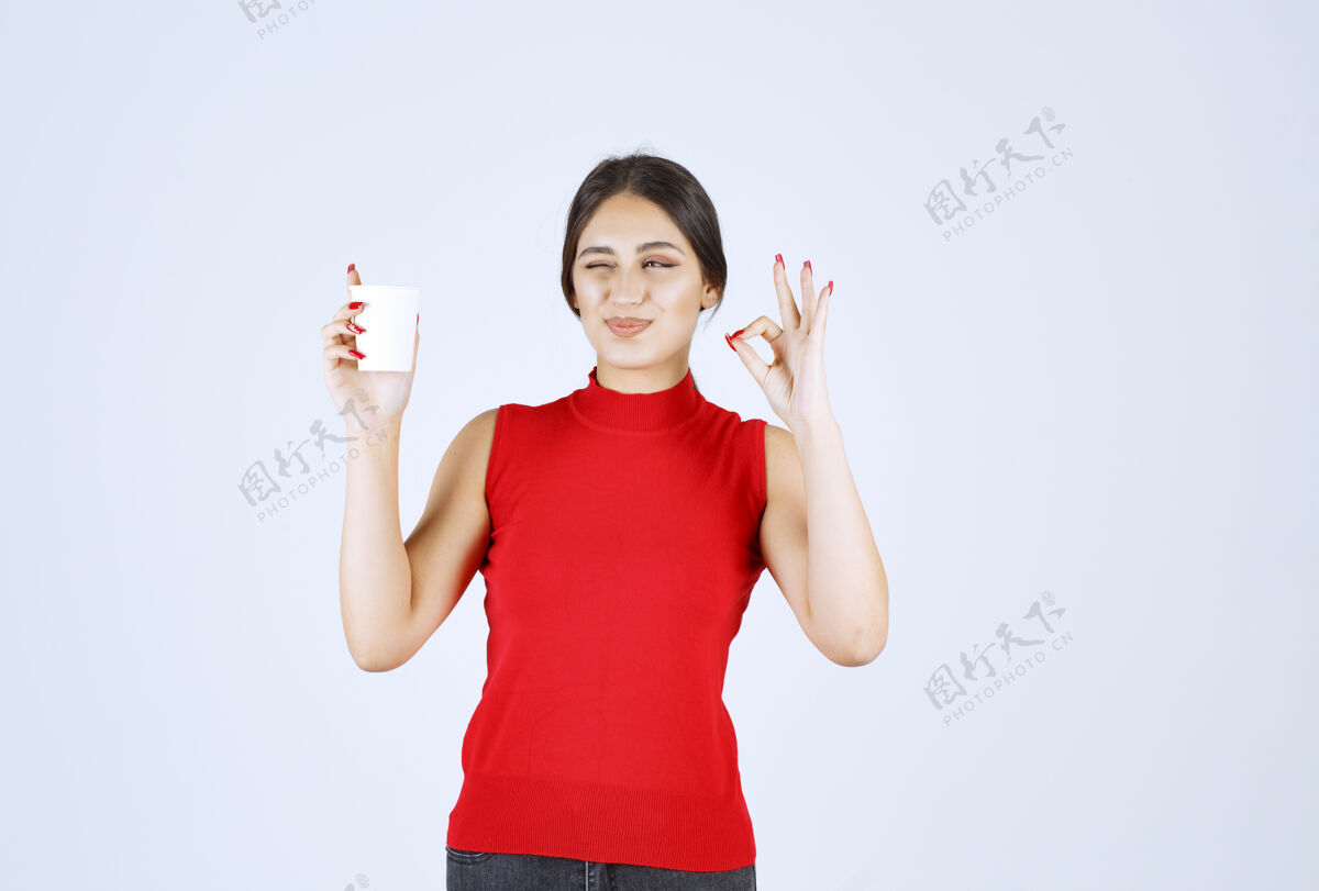 喜欢穿红衬衫的女孩在喝咖啡 并表现出积极的迹象工人姿势美味