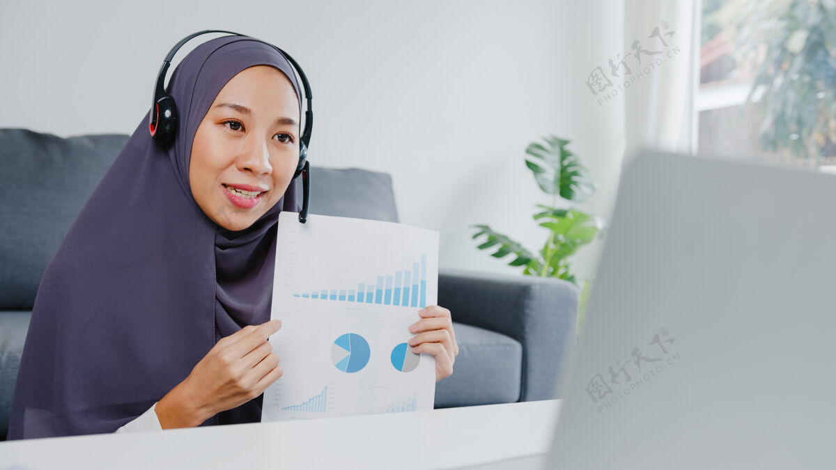学习穆斯林女士戴着耳机用笔记本电脑在客厅工作时通过电话会议和同事谈论销售报告头巾学习耳机