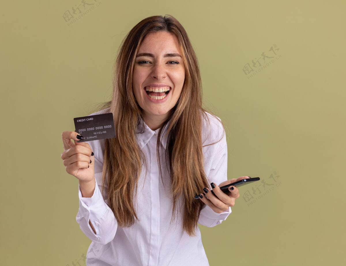 美丽快乐的年轻漂亮的白人女孩拿着信用卡和电话欢乐绿色年轻