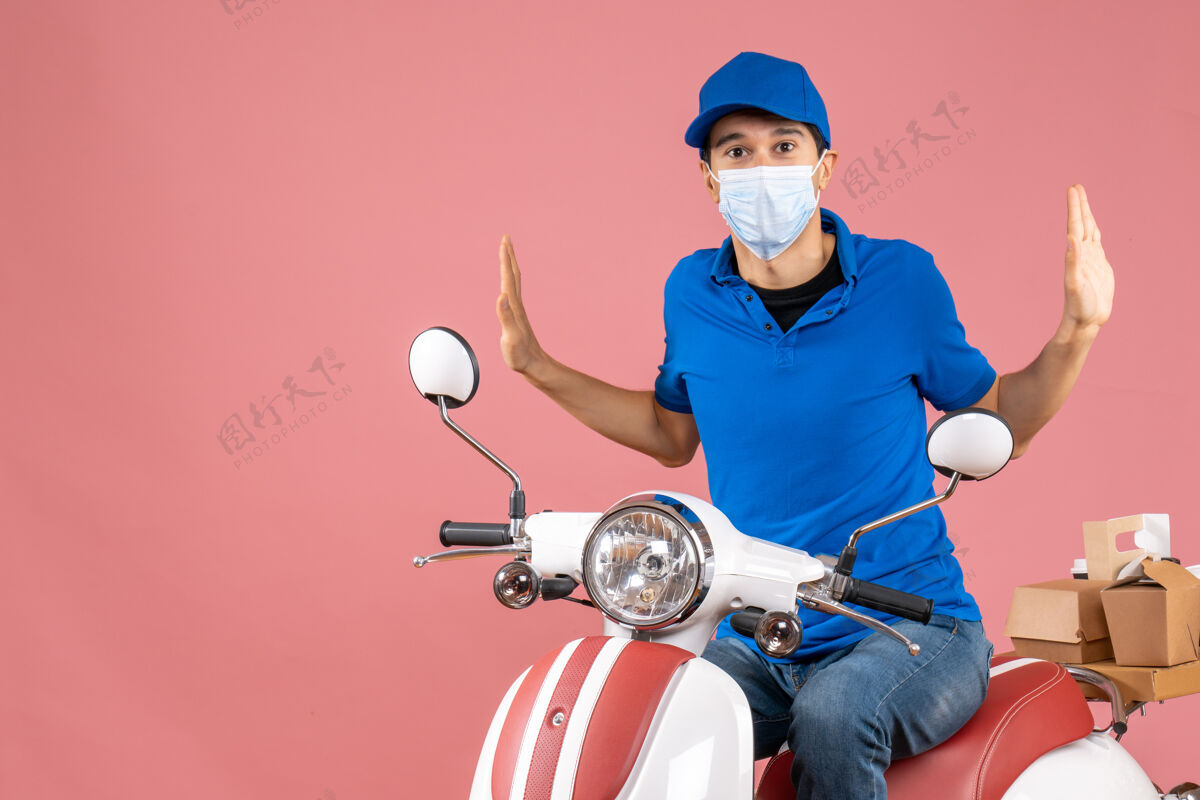 头盔顶视图混乱的快递员戴着医疗面具戴着帽子坐在粉彩桃色背景的踏板车上坐着头盔粉彩