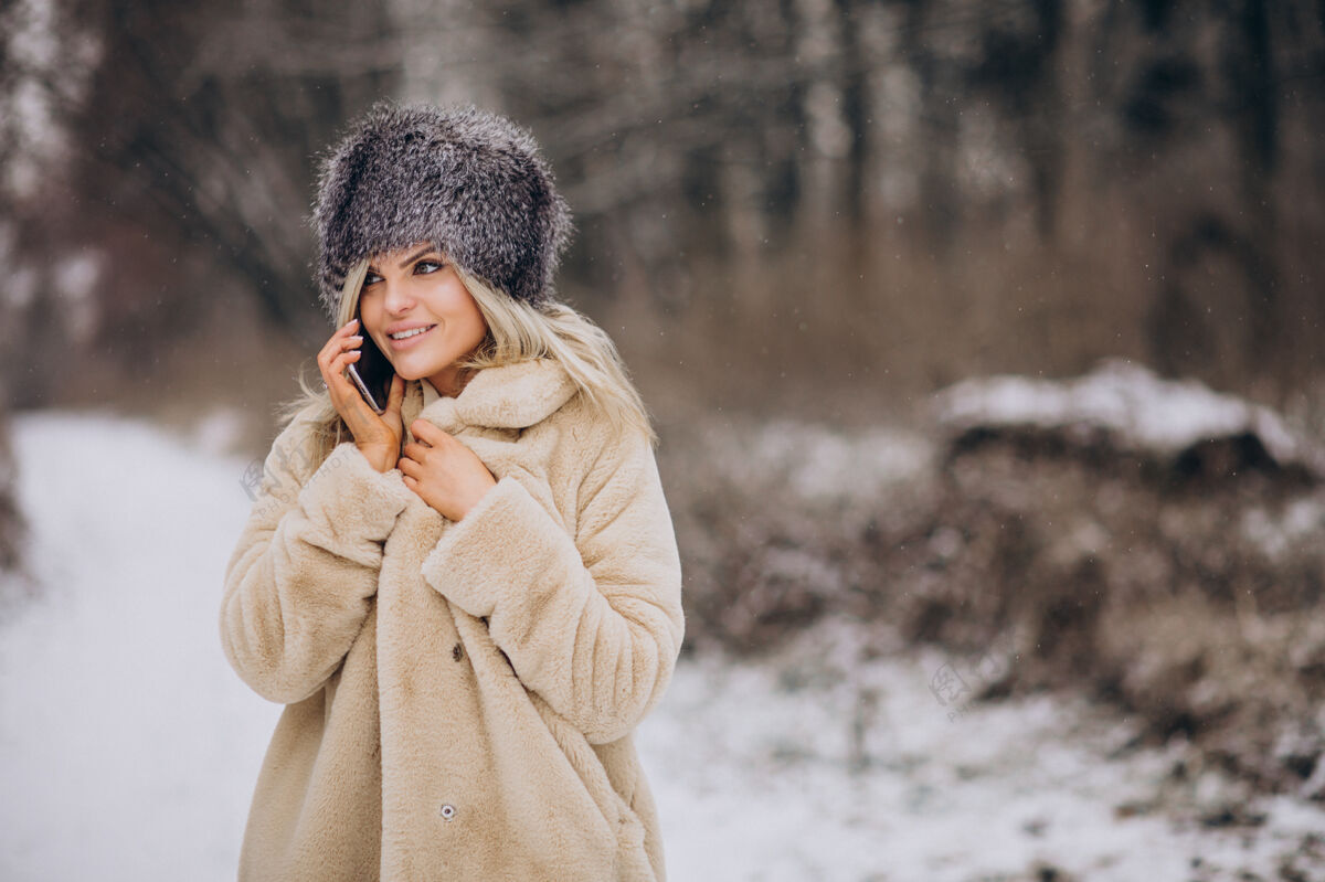 降雪穿着冬衣的女人走在满是雪的公园里打电话树移动探索
