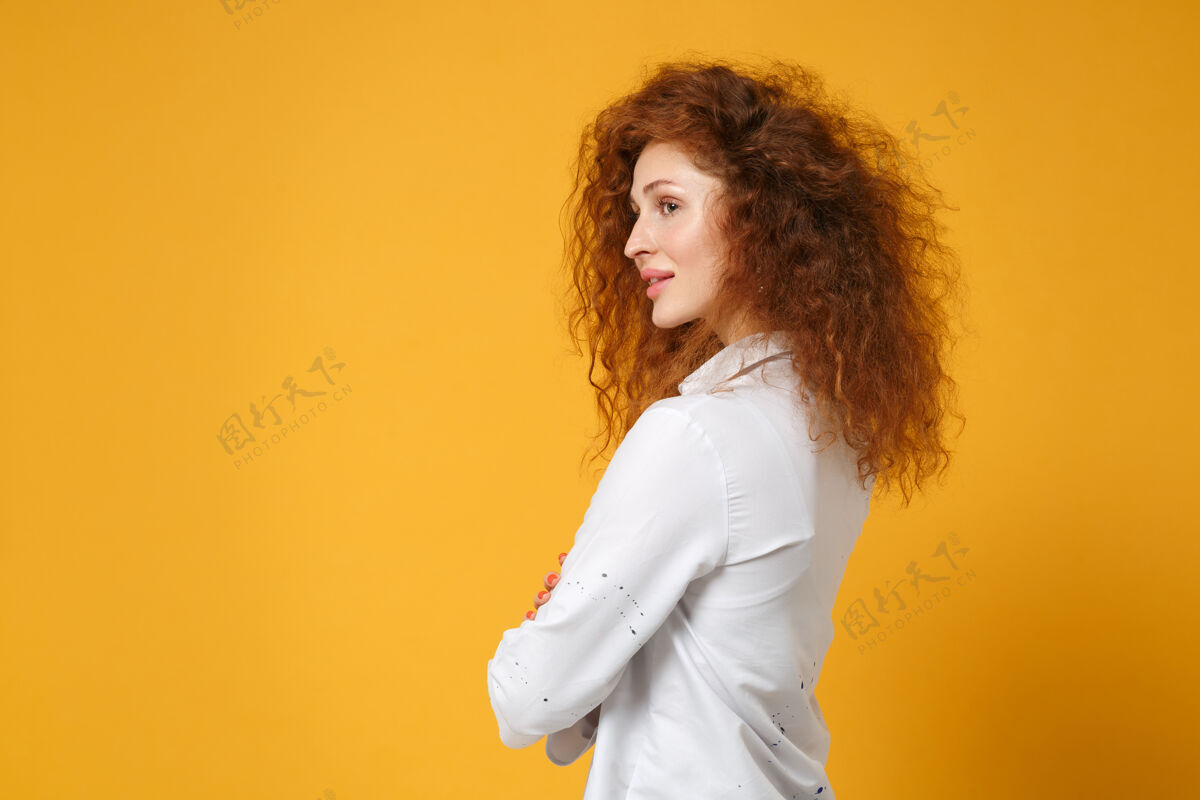 卷发侧视图美丽的年轻红发女子女孩在休闲白衬衫摆出孤立的黄橙色墙上壁板脸手