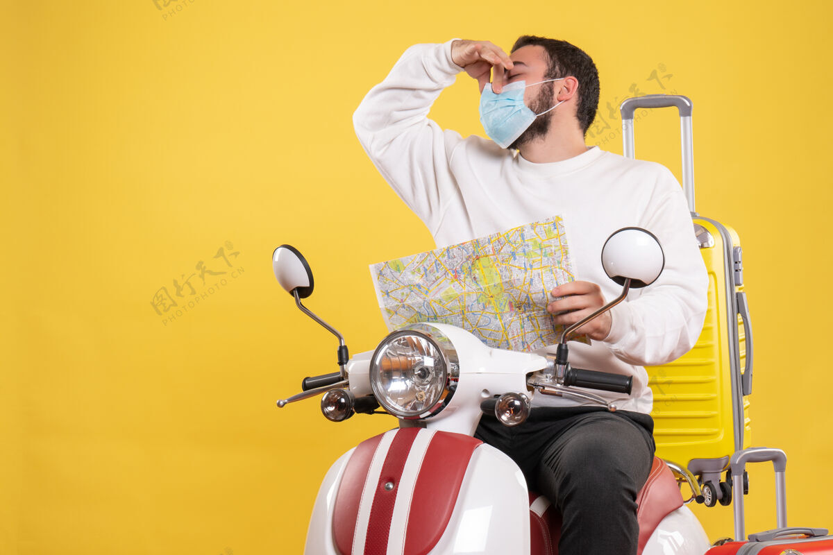 地图一个戴着医用口罩的年轻人坐在摩托车上 背着黄色的手提箱 拿着地图做着臭味手势球员坏运动