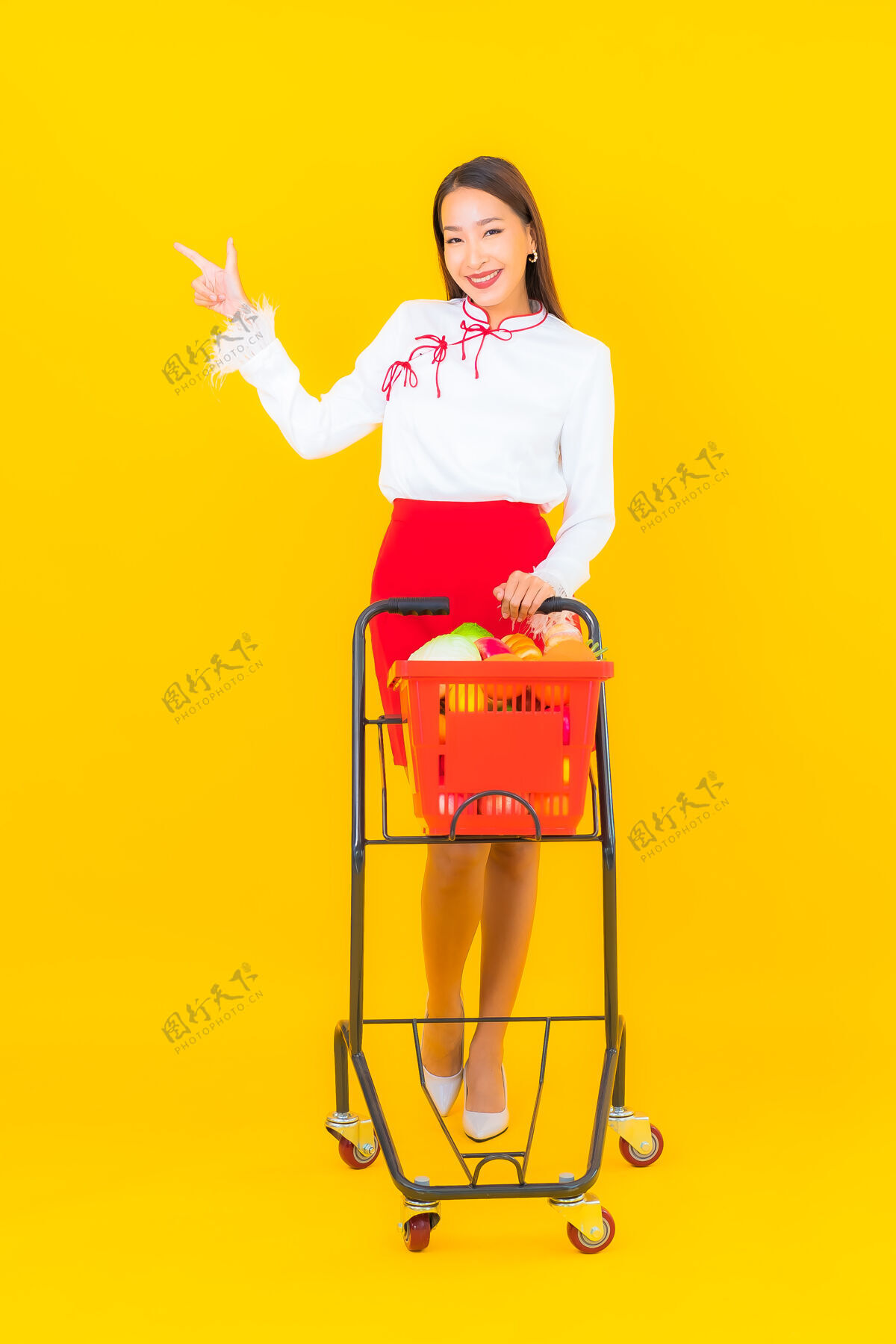 杂货店一幅美丽的亚洲年轻女子的画像 黄色的是超市里的购物篮女性购买购物车