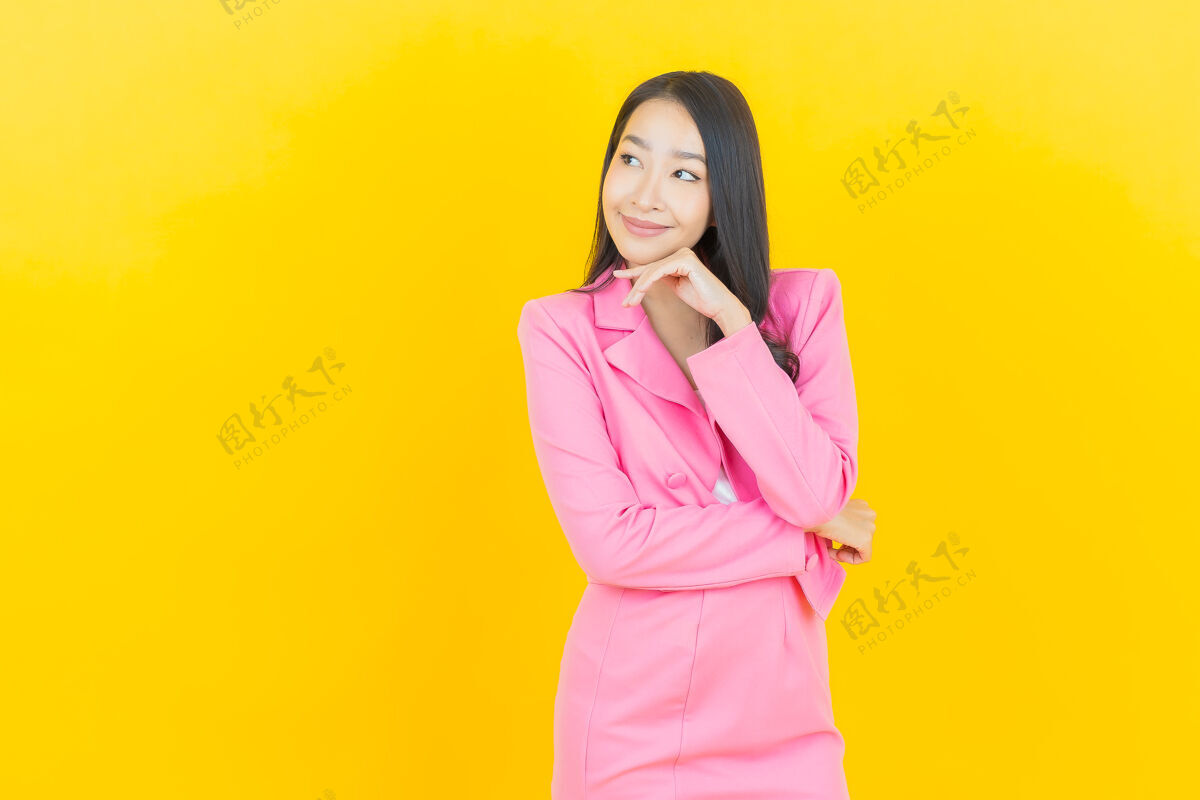 亚洲人在黄色墙壁上描绘美丽的亚洲年轻女子微笑的动作穿着漂亮模特