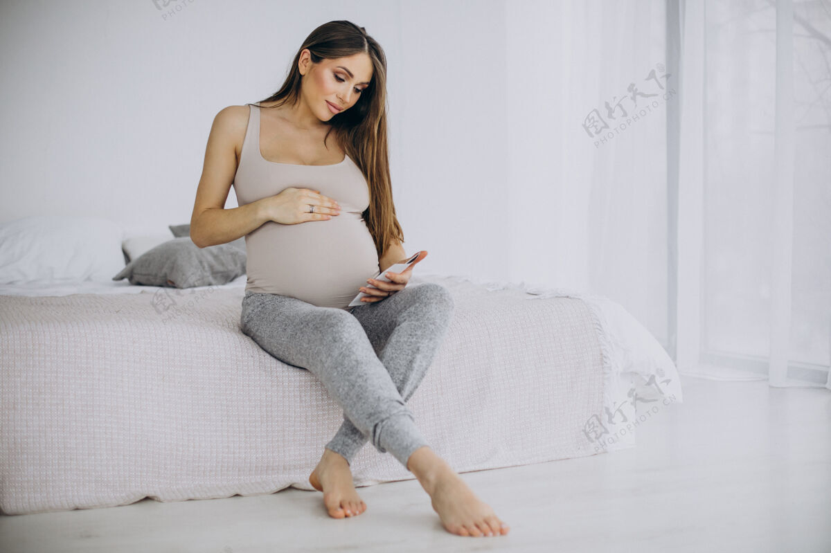 等待孕妇带着超声波照片坐在床上产前报告超声波