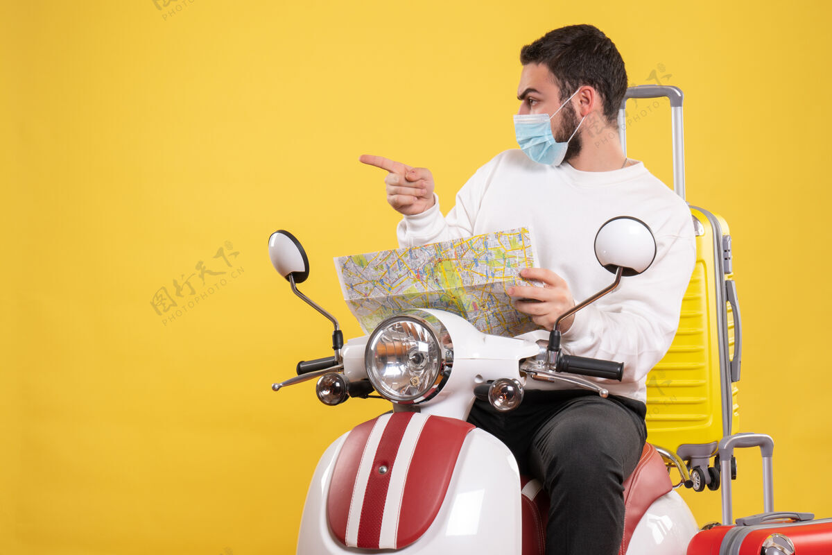 人带着医用面罩的好奇的家伙坐在摩托车上 带着黄色的手提箱 在黄色的地图上展示旅行概念坐着手提箱黄色
