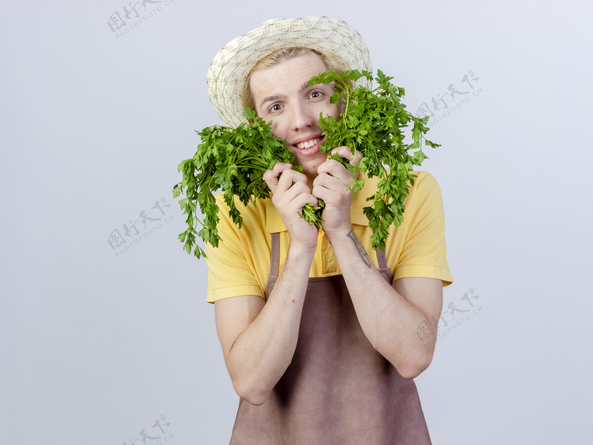 快乐年轻的园丁 穿着连体衣 戴着帽子 手里拿着新鲜的草药 脸上挂着微笑脸帽子穿
