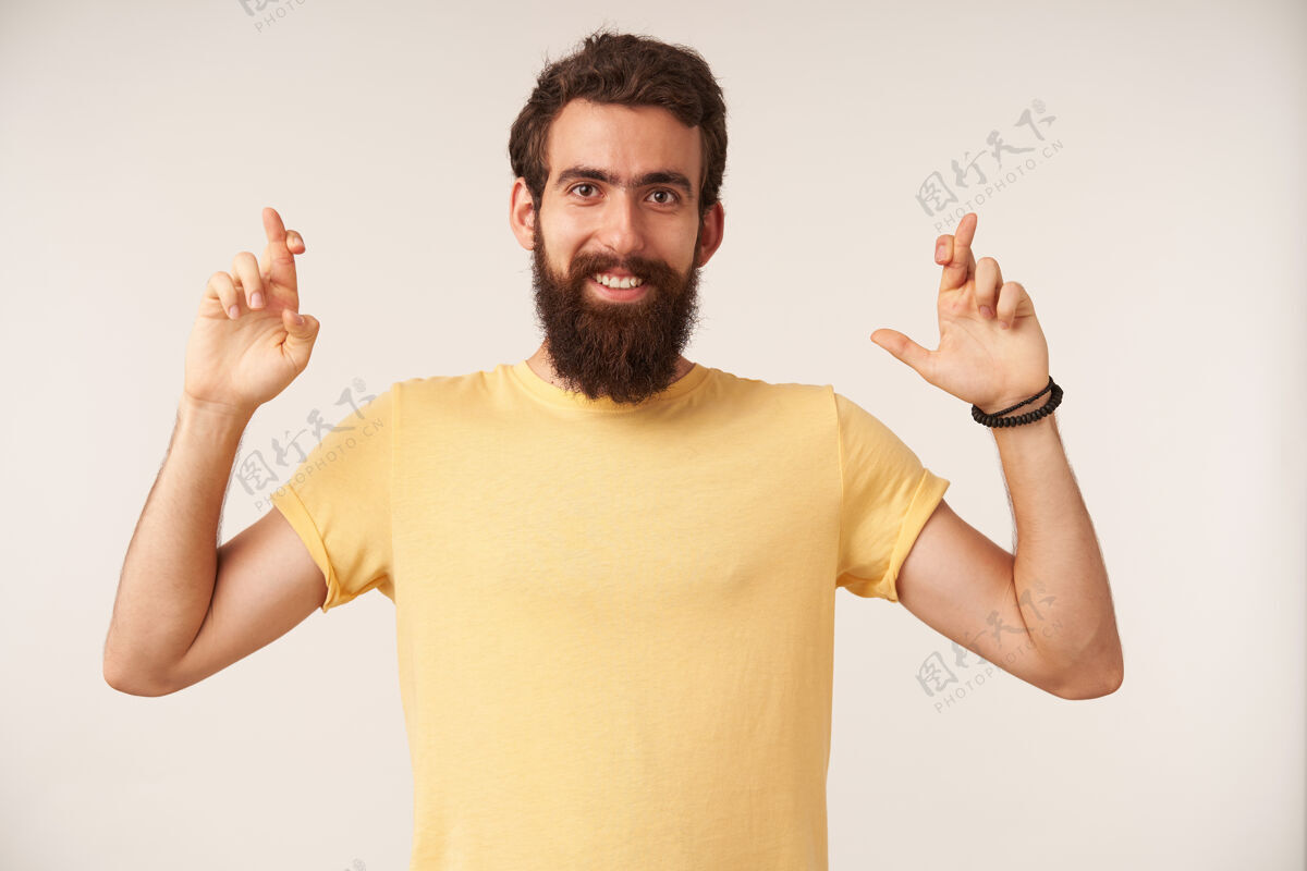 自信留着胡子的年轻人的肖像 穿着黄色t恤休闲风格 交叉着手指站着墙姿势男人