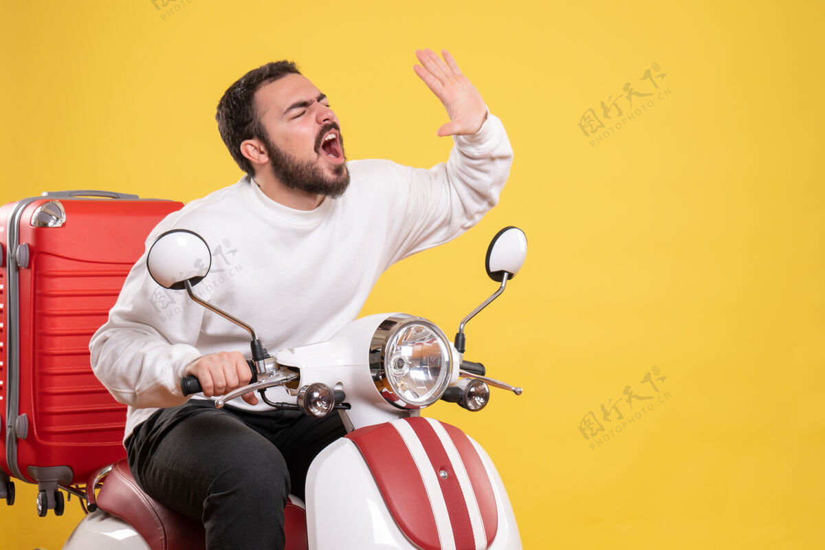 手提箱俯视图：紧张的年轻人坐在摩托车上 提着手提箱 在孤立的黄色背景下呼唤着某人人成人运动