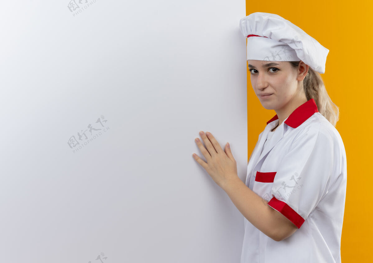 墙自信的年轻漂亮厨师穿着厨师制服站在旁边 把手放在白色墙壁上 隔离在白色墙壁上 留有复印空间手靠近制服