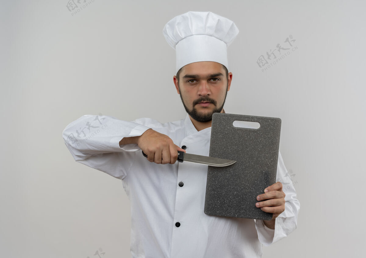 刀自信的年轻男厨师身着厨师制服 手拿菜板和刀子隔离在白色的墙上持有信心板