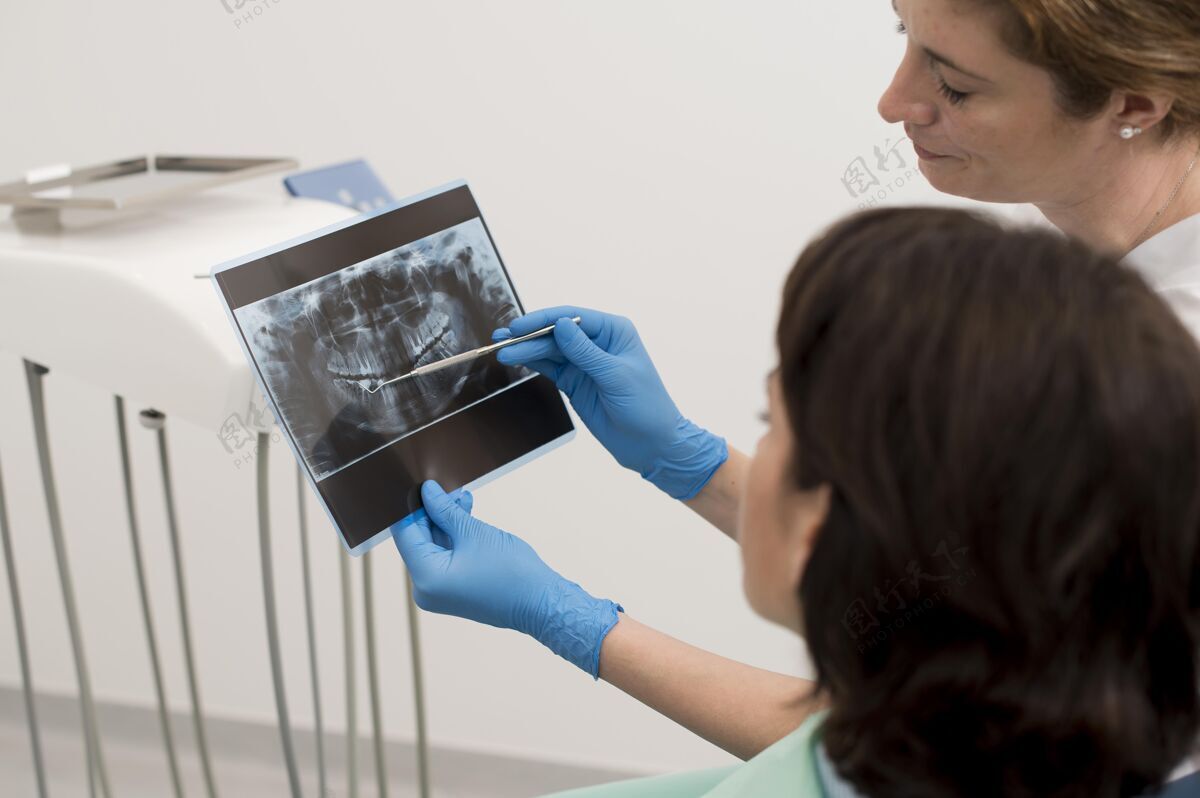 射线照相女病人和牙医一起看牙齿的X光片工人专业X光