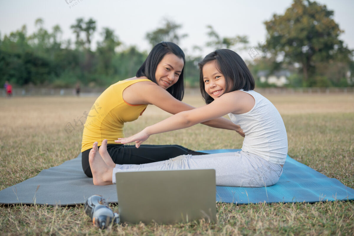 体育妈妈和女儿在做瑜伽在公园里训练妇女和孩子户外运动健康的运动生活方式 在线观看瑜伽练习视频教程和坐姿前弯姿势积极锻炼一起