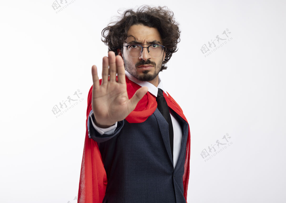 男人自信的年轻白种人超级英雄 戴着眼镜 穿着西装 披着红色斗篷 示意停车牌眼镜超级英雄复制