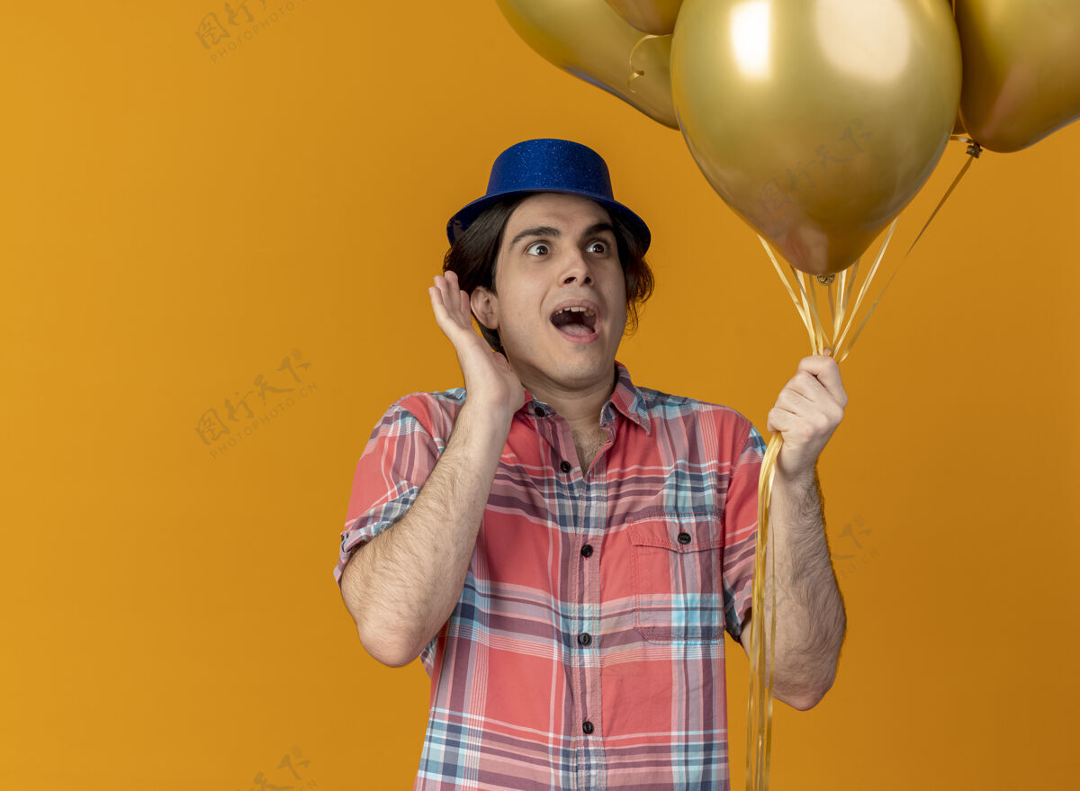 站兴奋的白人帅哥戴着蓝色的派对帽站着 手举着氦气球男人复制气球