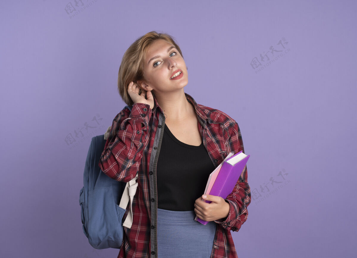年轻高兴的年轻斯拉夫女学生背着书包拿着笔记本撩头发学生头发女孩