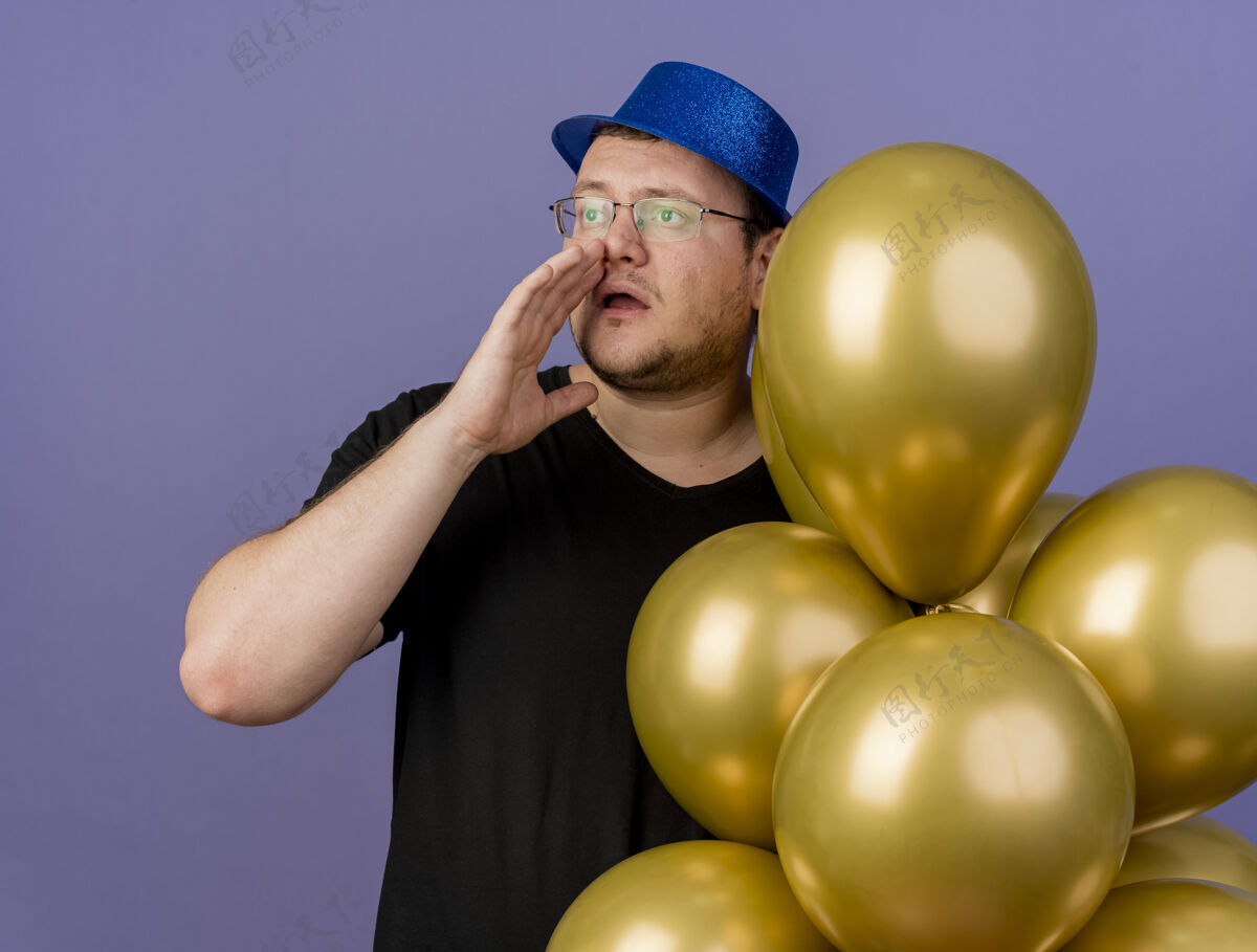 光学焦虑的成年斯拉夫人戴着眼镜 戴着蓝色的聚会帽 手紧靠着嘴 手里拿着氦气球戴成人保持