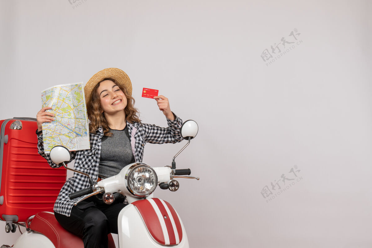 地图骑着轻便摩托车的漂亮年轻女子拿着灰色的卡片和地图摩托车肖像人