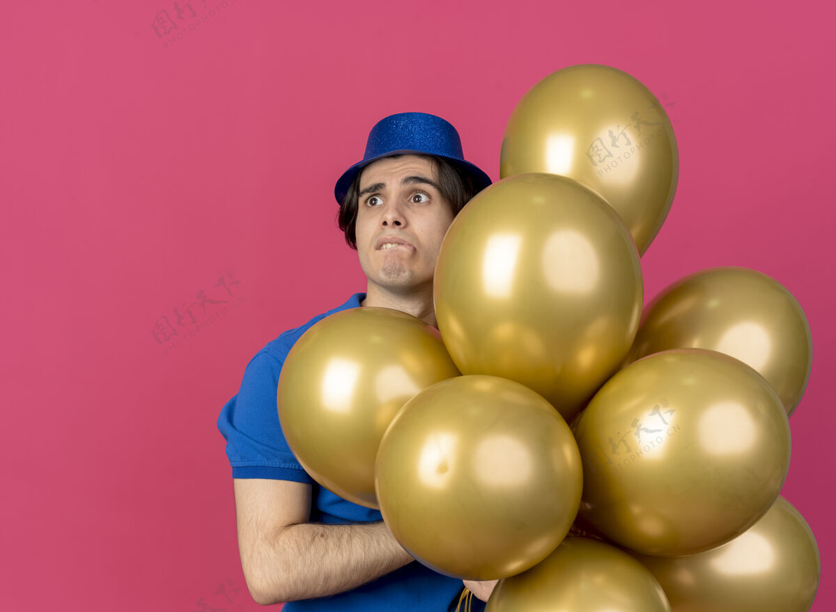 男人焦急英俊的白人男子戴着蓝色的派对帽手持氦气球望着身边壁板粉色焦虑